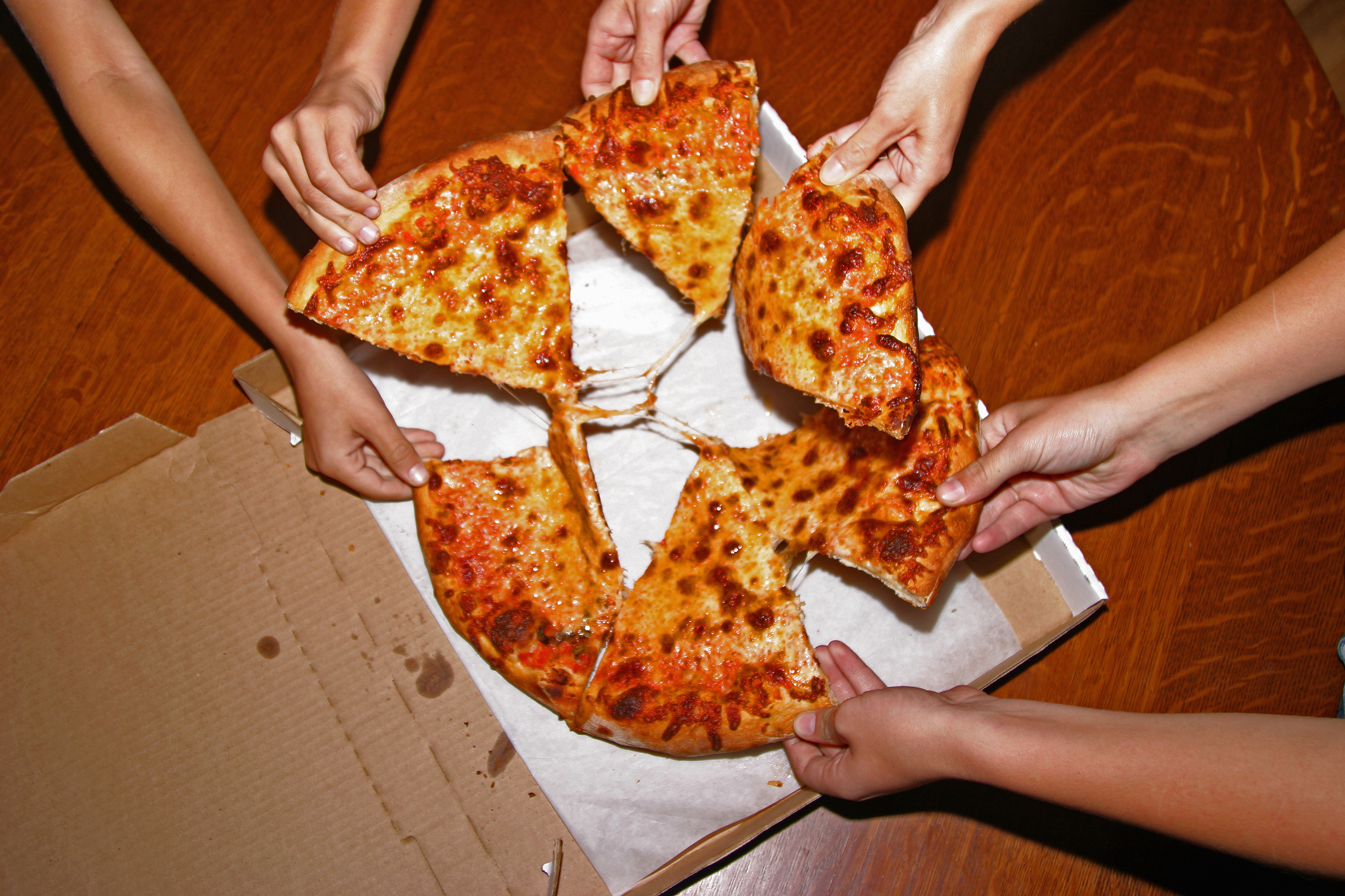 Several hands grabbing slices of pizza from a box