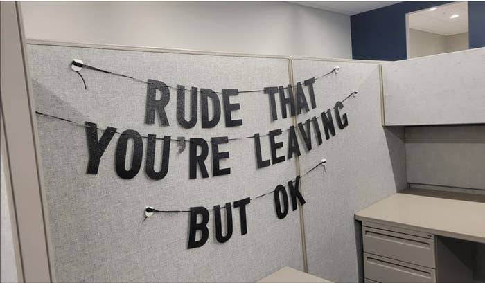 Banner across office cubicle reads &quot;RUDE THAT YOU&#x27;RE LEAVING BUT OK&quot;, possibly a coworker&#x27;s humorous farewell