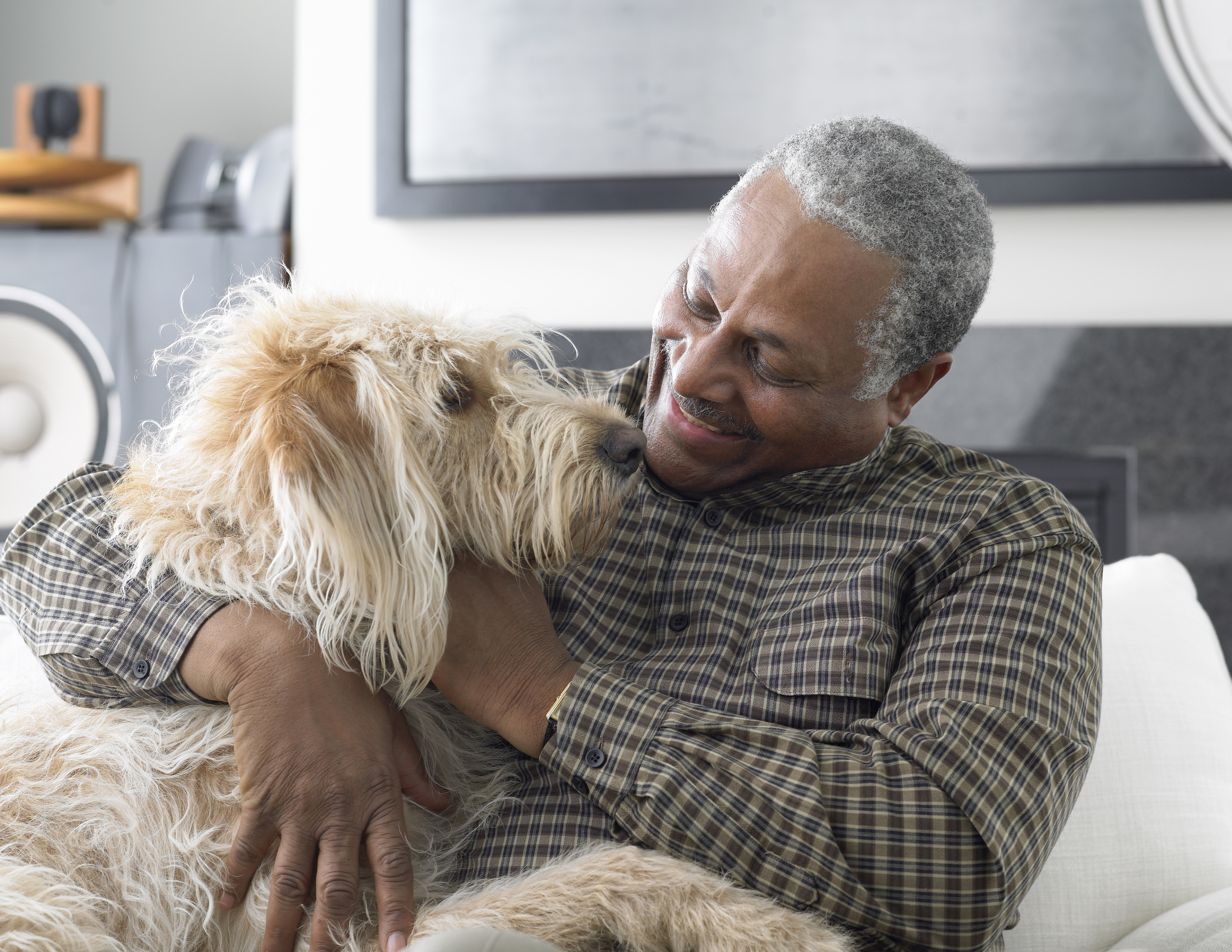 Man sitting on couch, smiling and embracing a fluffy dog, in a home setting