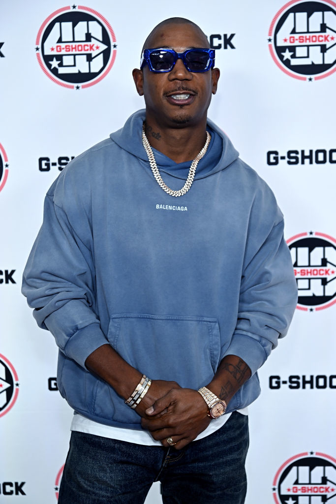 Ja Rule in a designer hoodie and sunglasses stands against a branded backdrop