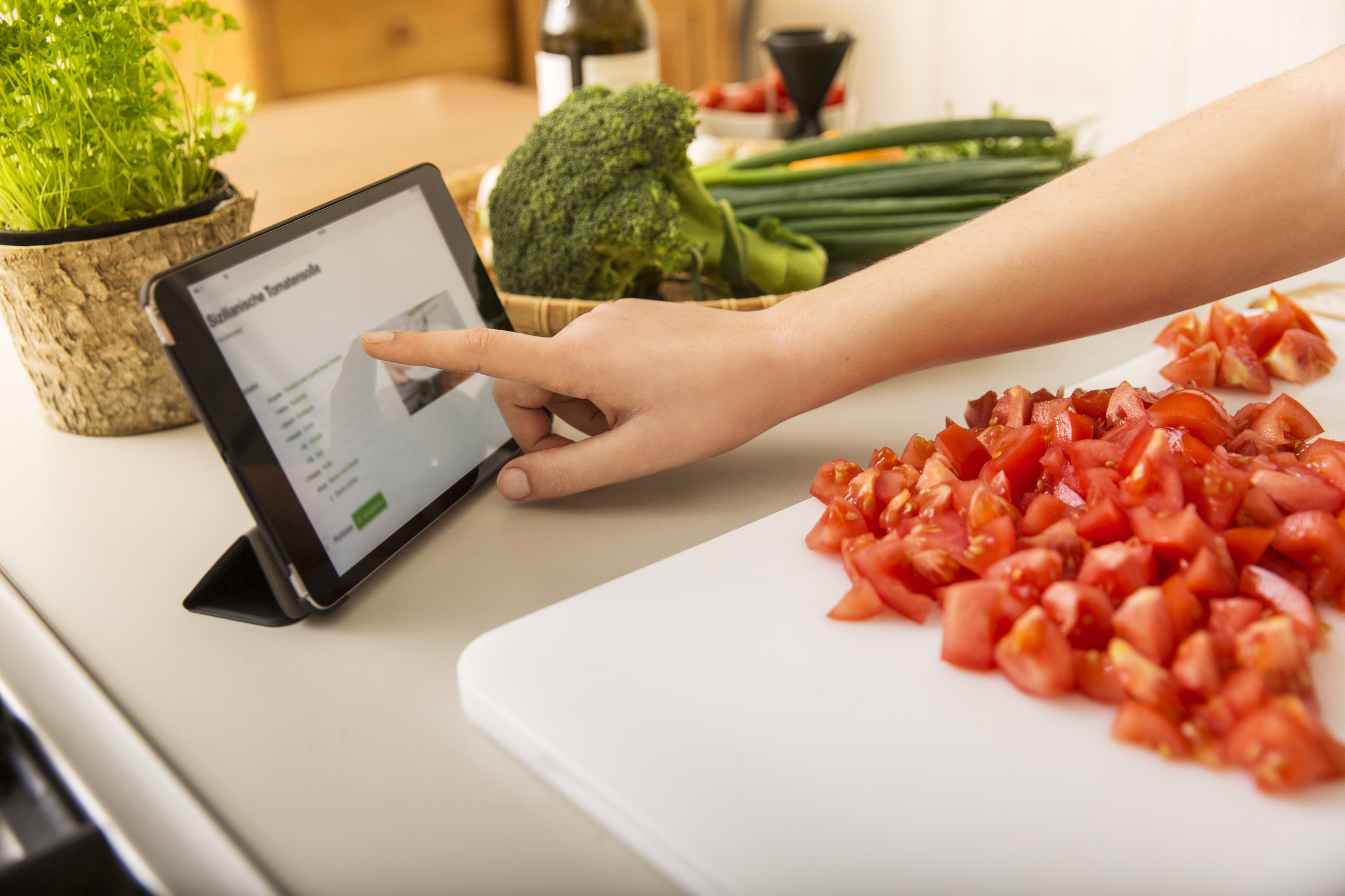 Person using a tablet with a recipe on screen while chopping tomatoes on a cutting board