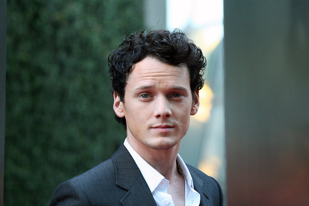 Anton Yelchin in a grey suit at an event with greenery in the background