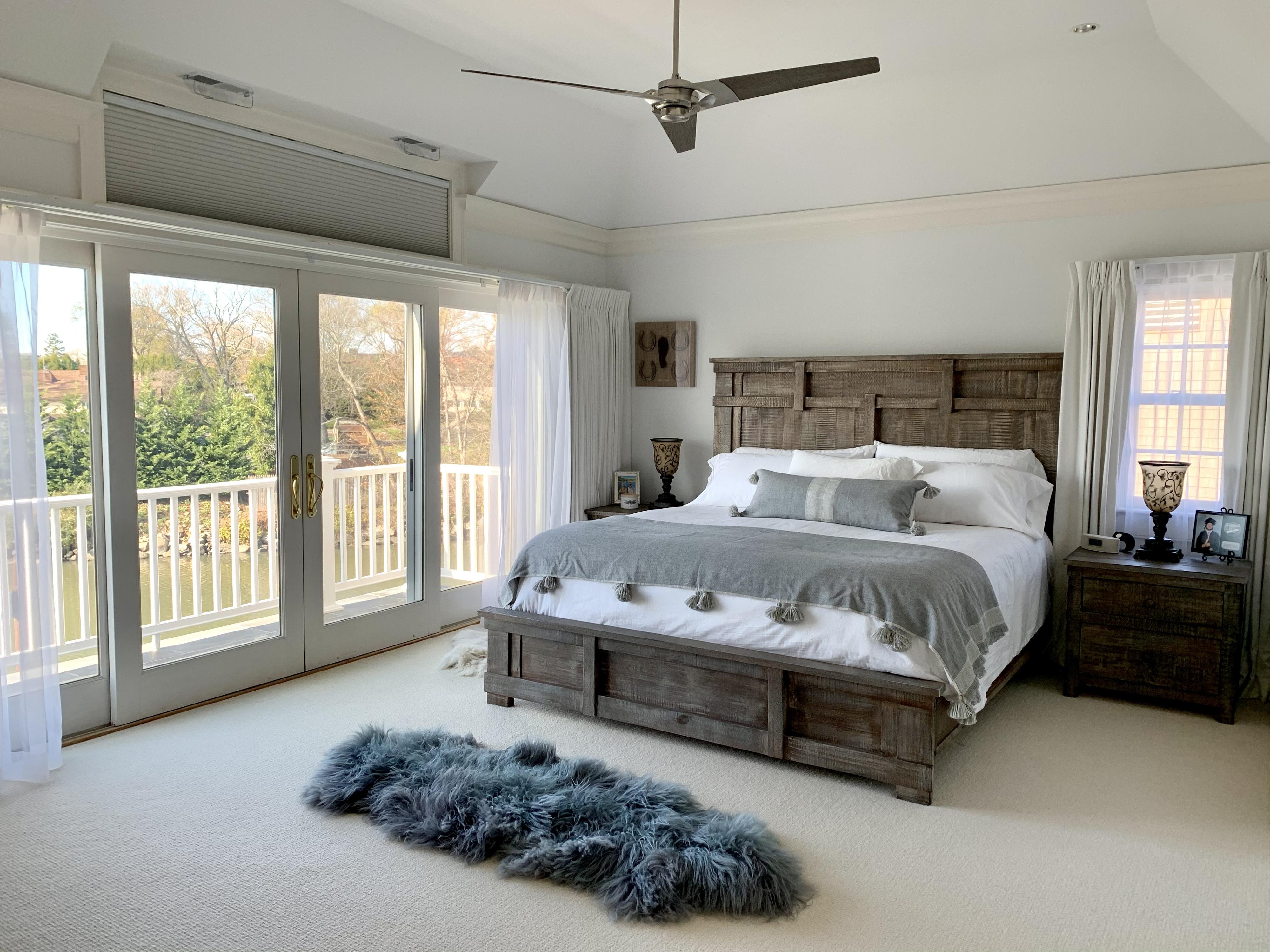 A well-lit bedroom with a large bed, wooden furniture, carpeting, and balcony doors
