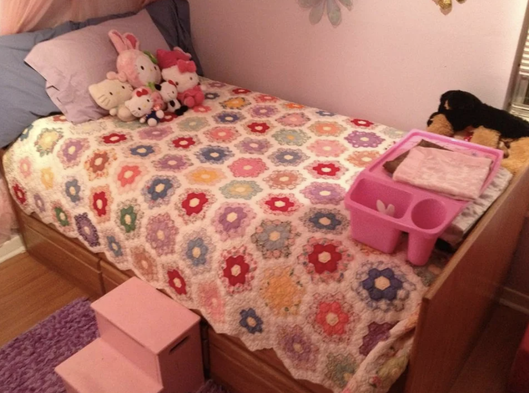 A childhood bedroom with a colorful quilt–covered twin captain&#x27;s bed, plush toys, and small pink steps on the side of the bed