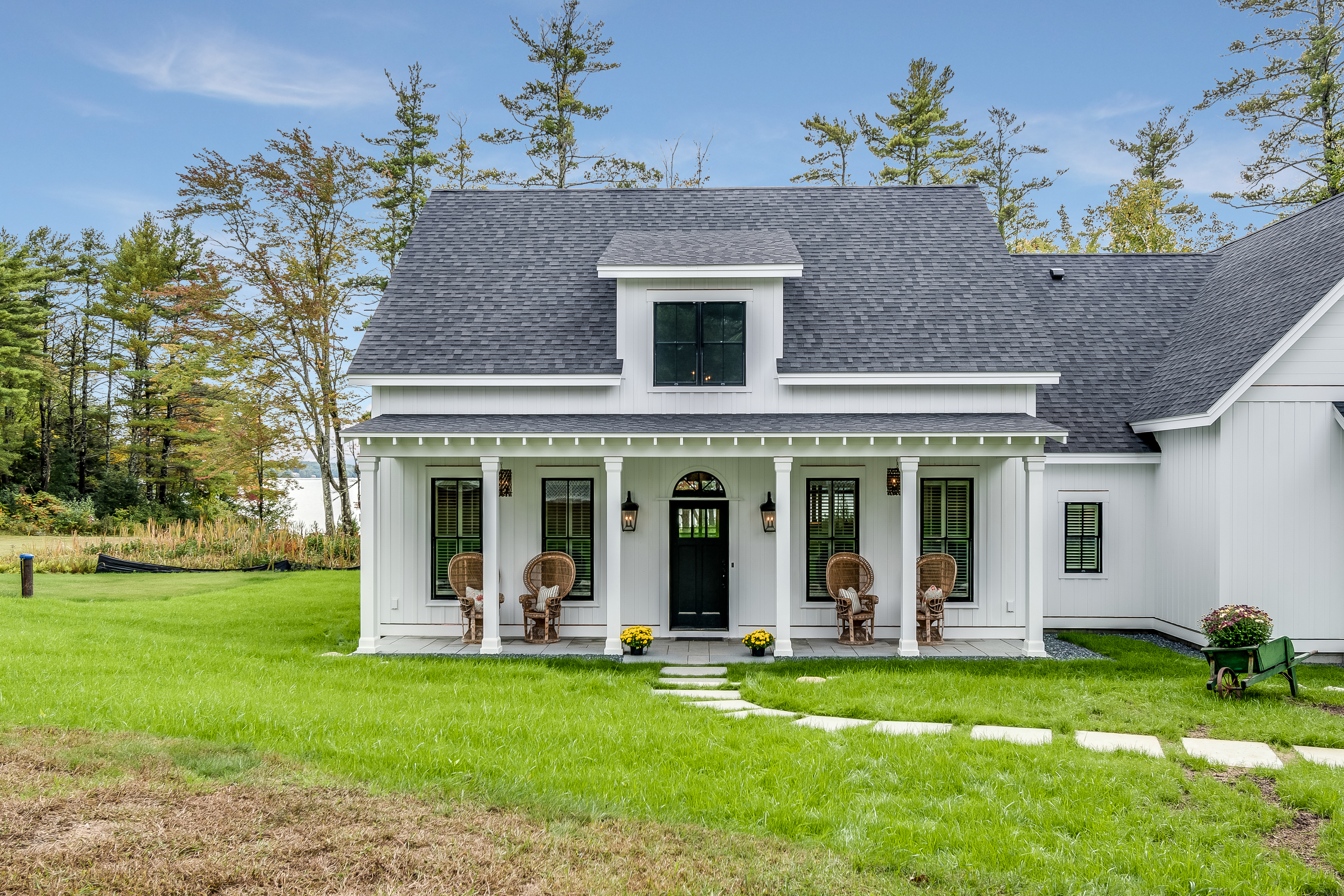 A small white house with a black roof, front porch with chairs, and a manicured lawn