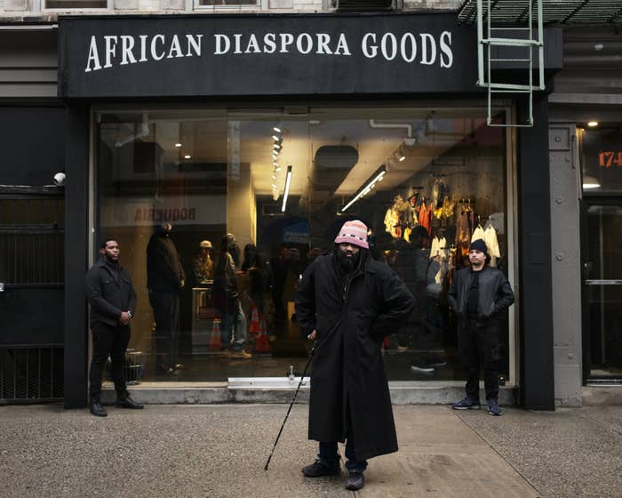 Three people outside a store named &#x27;AFRICAN DIASPORA GOODS,&#x27; one with a cane in stylish attire