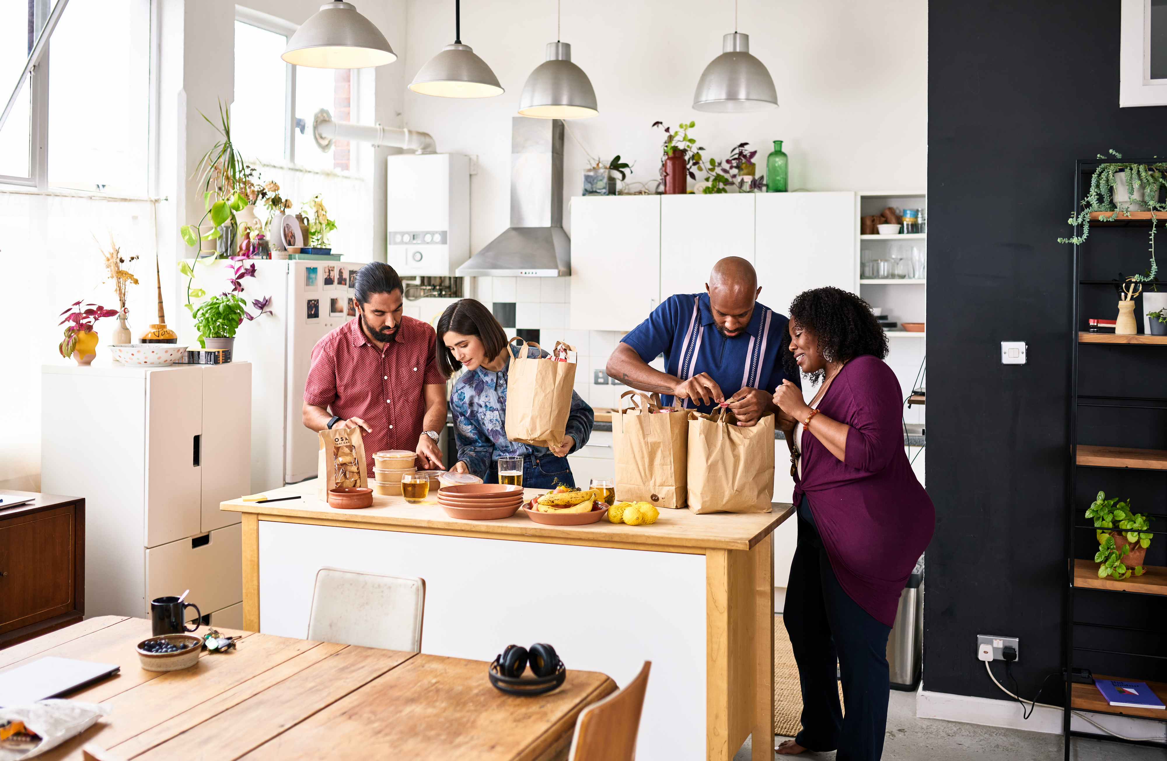 Four people unpacking groceries in a bright kitchen