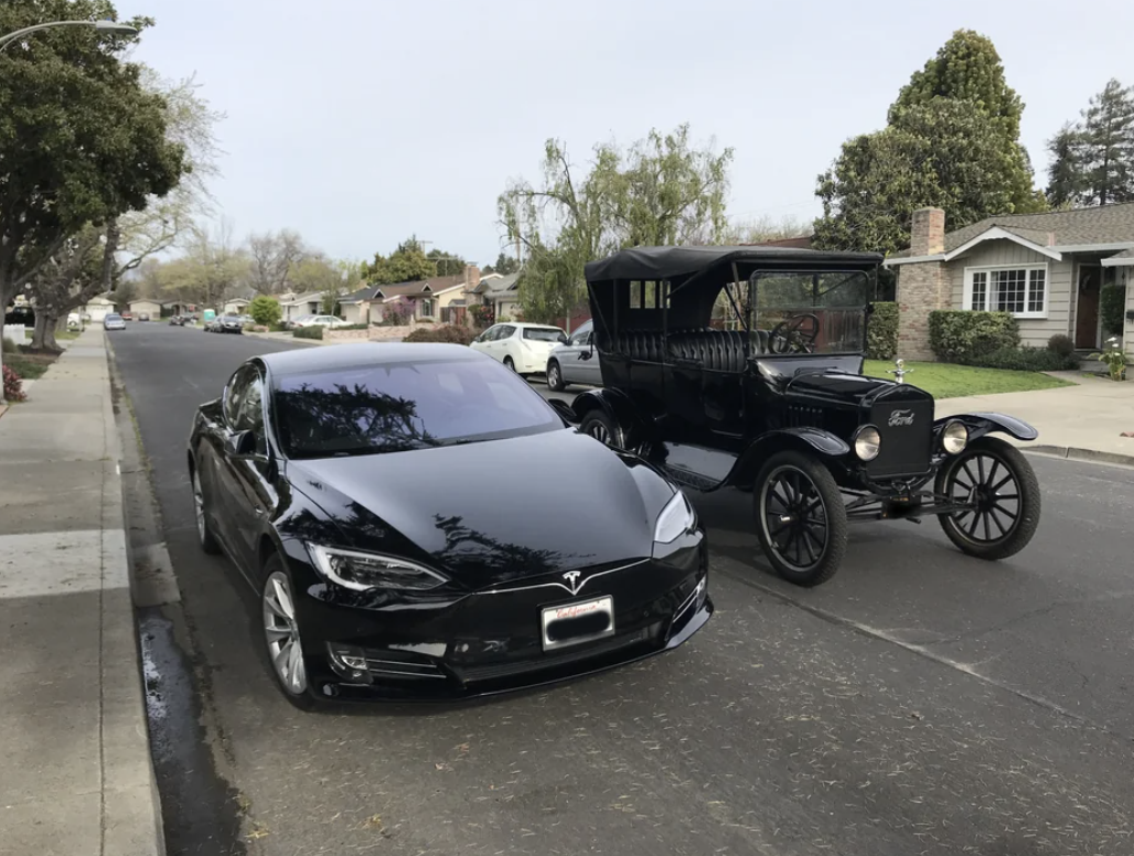 A modern Tesla parked next to a vintage Ford Model T on a suburban street, showcasing the evolution of automotive design