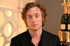 Man in a black suit with curly hair looking at the camera
