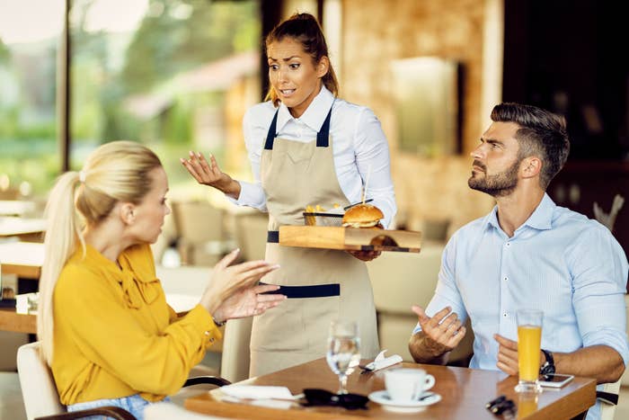 Waitress bringing food to a male and female diner at a restaurant, both appear to be in conversation with her