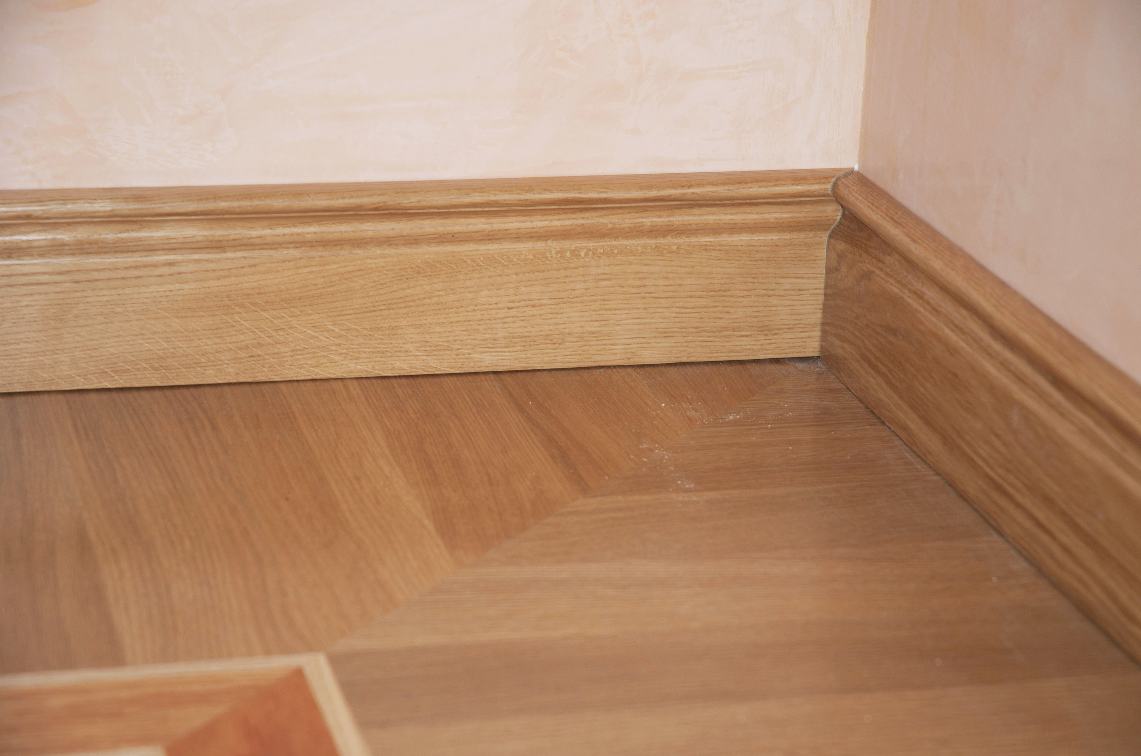 Wooden baseboard meeting a laminate floor in the corner of a room