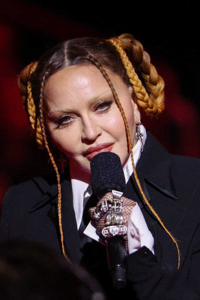 Madonna wearing a suit and braids, holding a microphone, performing on stage