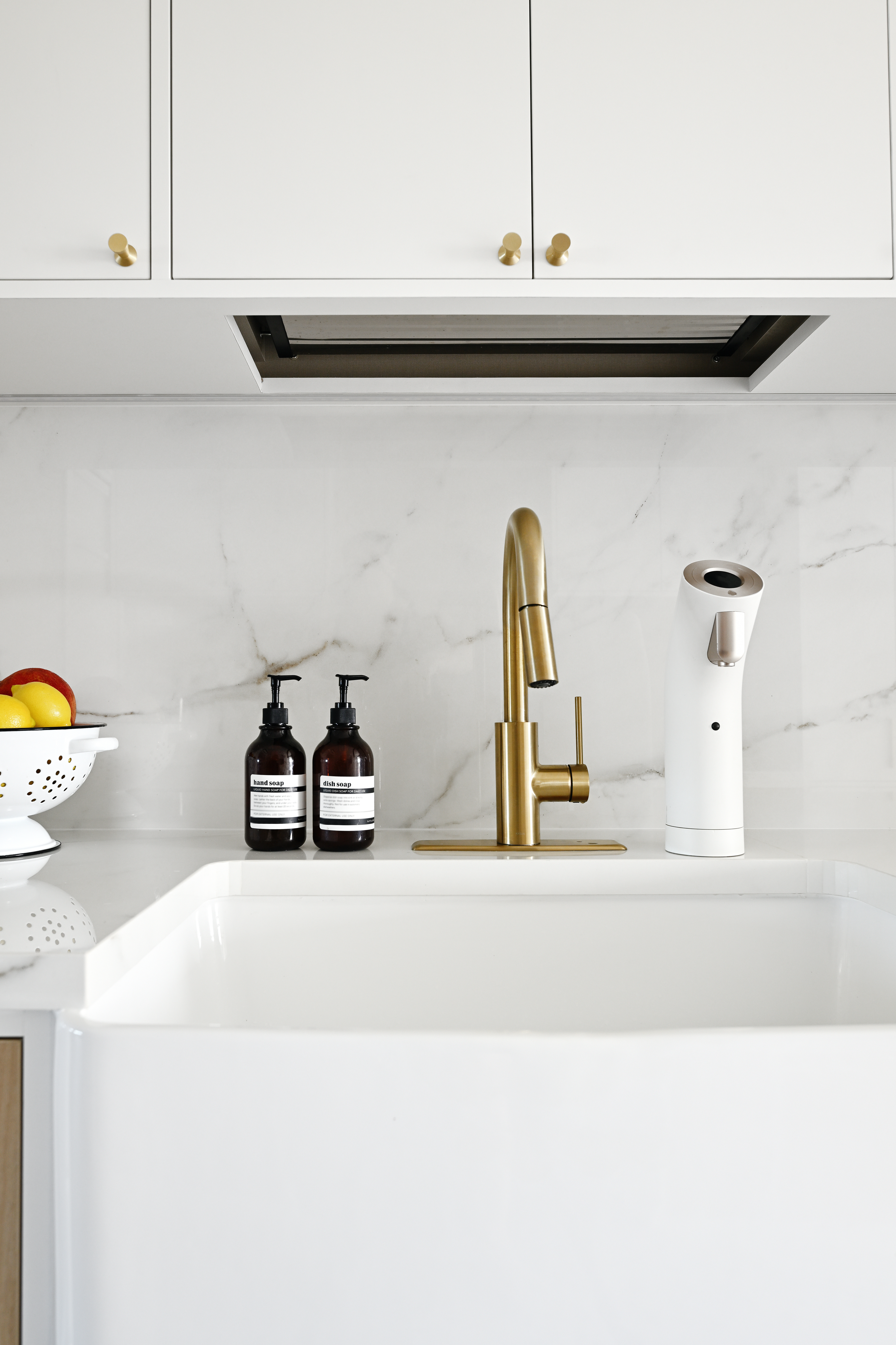 Large, modern kitchen sink with gold faucet, soap dispensers, and fruit bowl on the counter