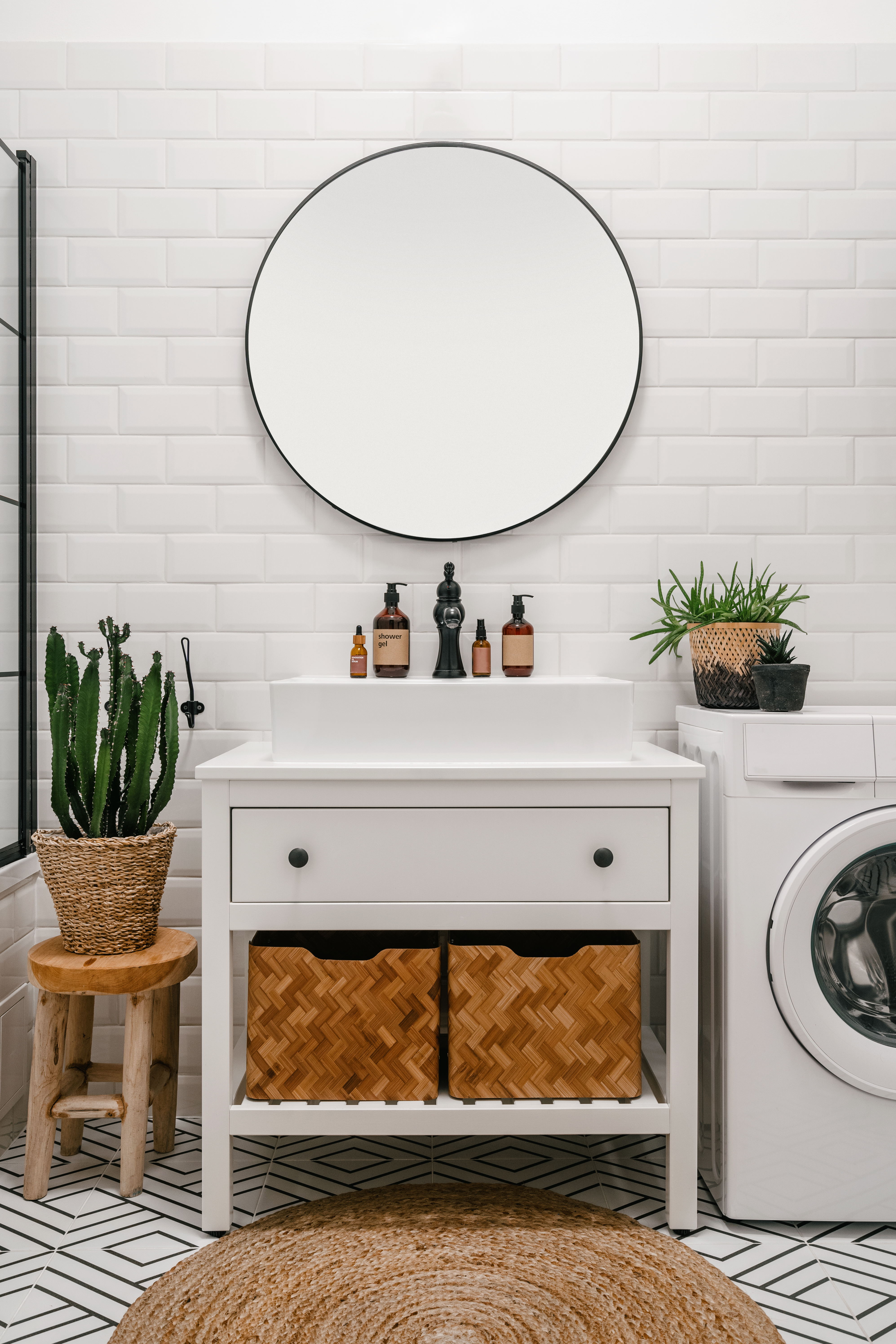 A modern bathroom with a round mirror, sink vanity, woven baskets, and a washing machine next to a potted plant