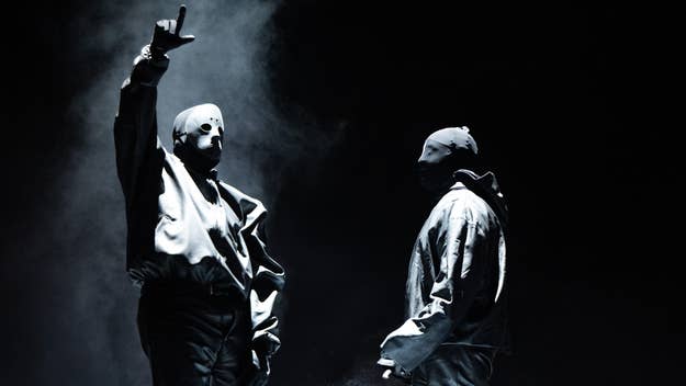 Two masked musicians on stage, one with arm raised, in a moody, smoke-filled performance