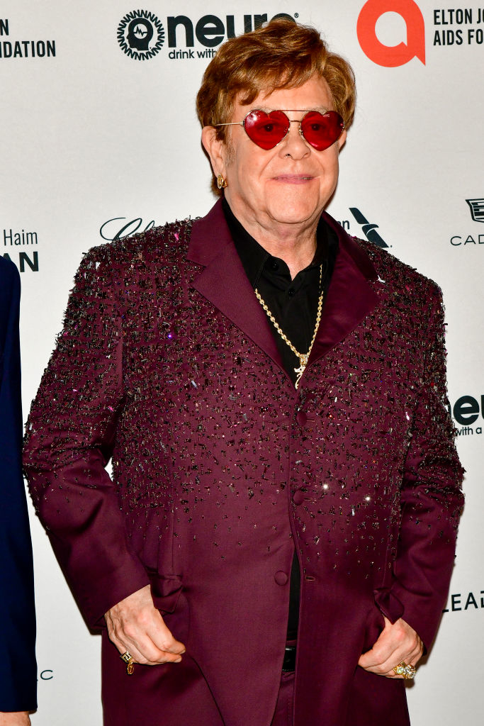 Elton John in a sparkly burgundy suit and sunglasses at an event