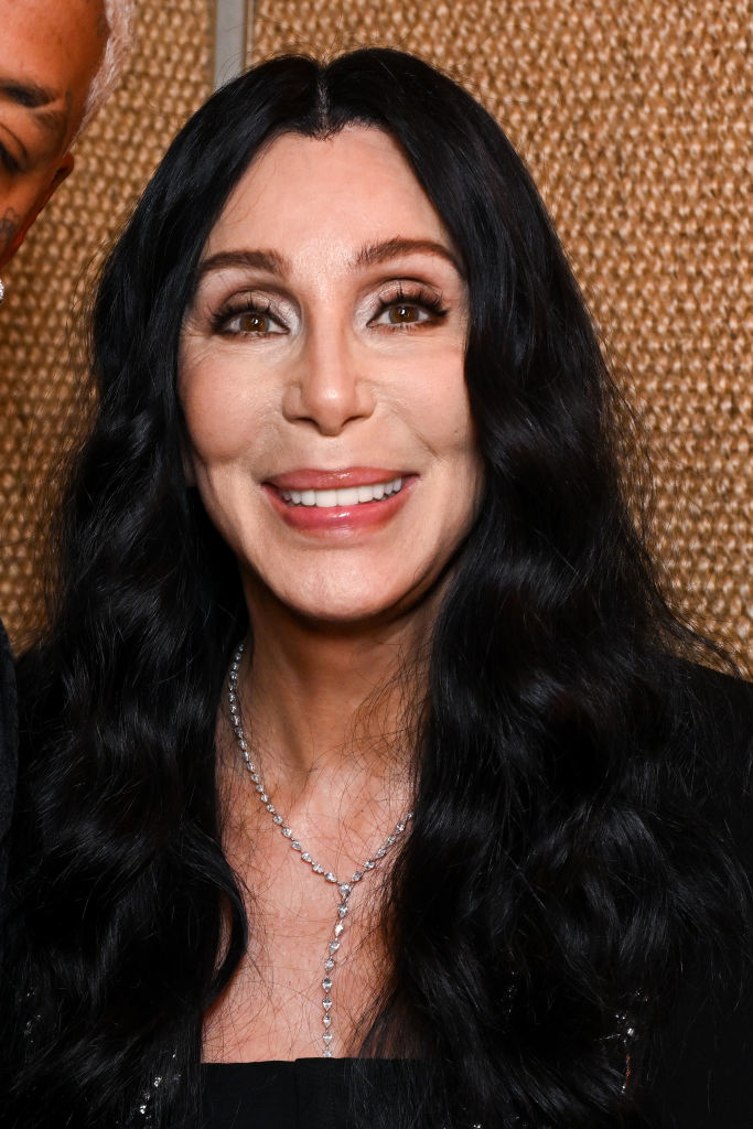 Cher in black attire with straight long hair, smiling at an event