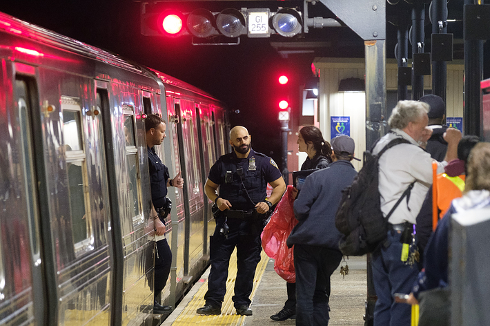 Police officer and passengers at a train station platform with open train doors