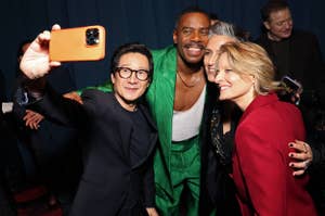 Three people pose for a selfie, with one holding the phone. They are smiling and dressed in formal attire