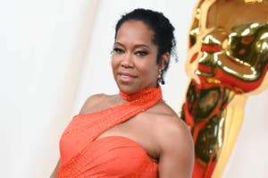 Regina King in a one-shoulder gown with beadwork, posing next to an Oscar statue