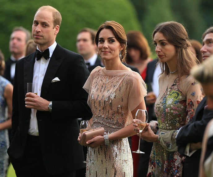 Prince William and Kate Middleton in formal attire at an outdoor event, with others around. Kate in a beaded dress