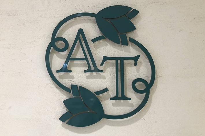 壁に取り付けられた「AT」のロゴ。装飾的な葉がデザインに含まれています。