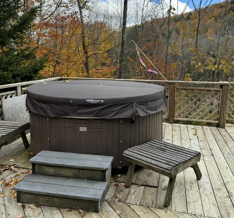 Backyard with a hot tub and wooden furniture amidst autumn trees