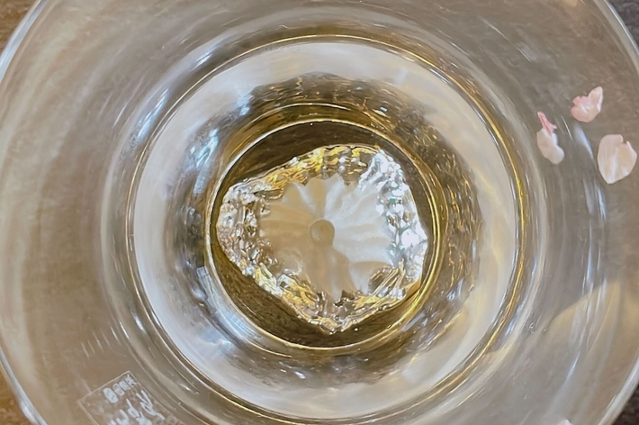 ガラスの器に入った透明な液体と散らばる花びら