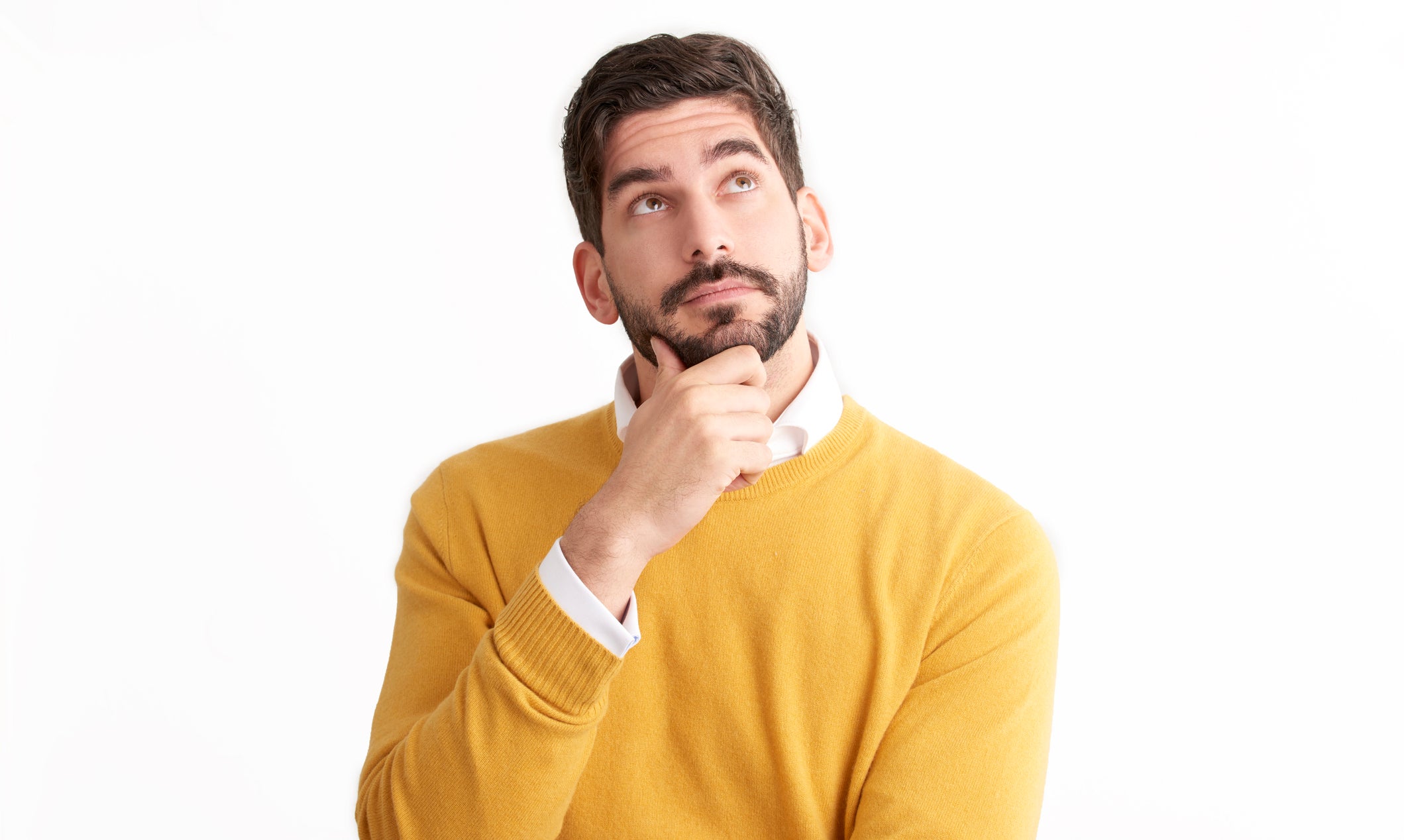 Man in yellow sweater looking up thoughtfully with hand on chin