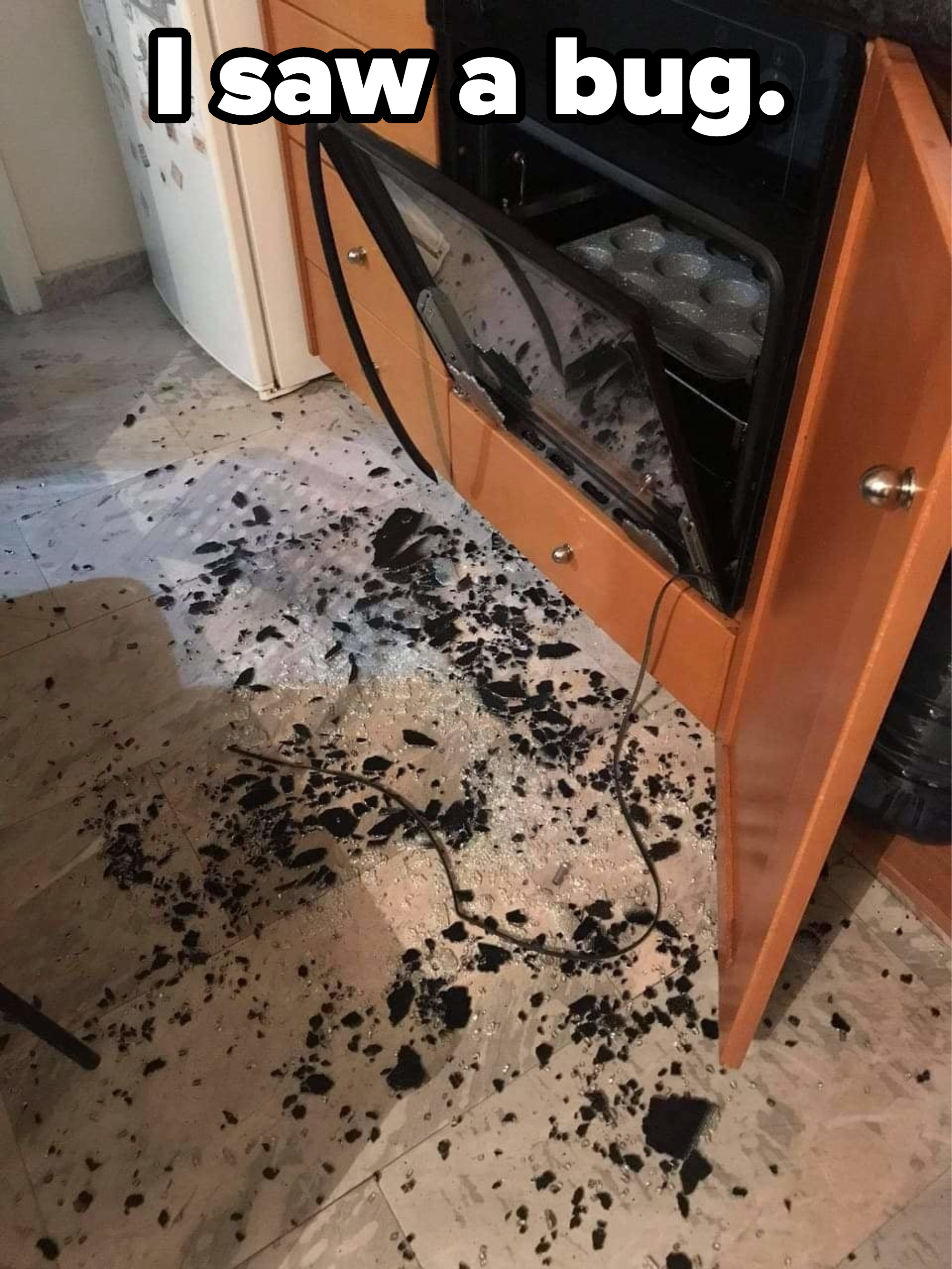 An oven door is open with shattered glass on the floor