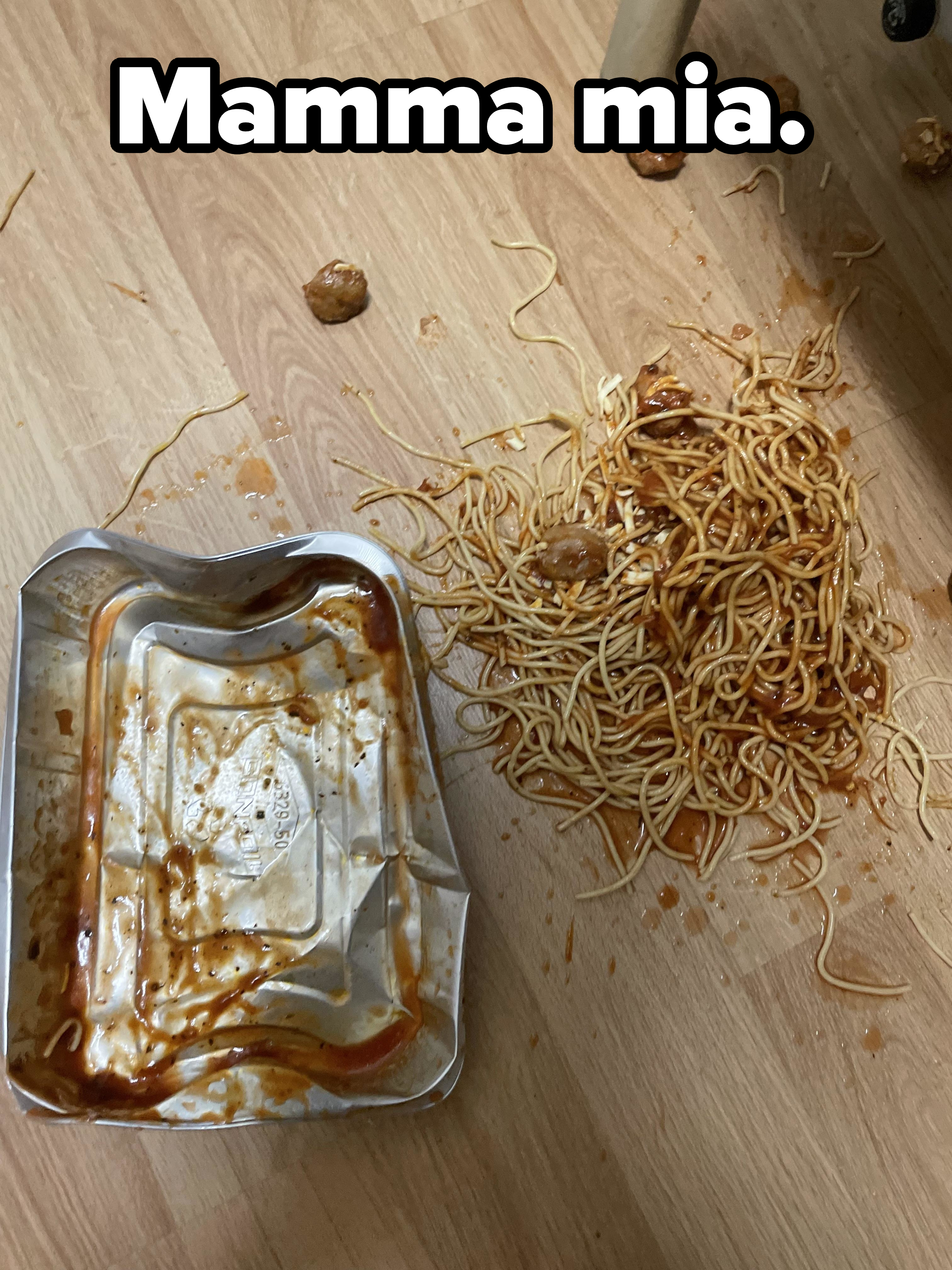 Spilled spaghetti and meatballs and an empty container on a wooden floor