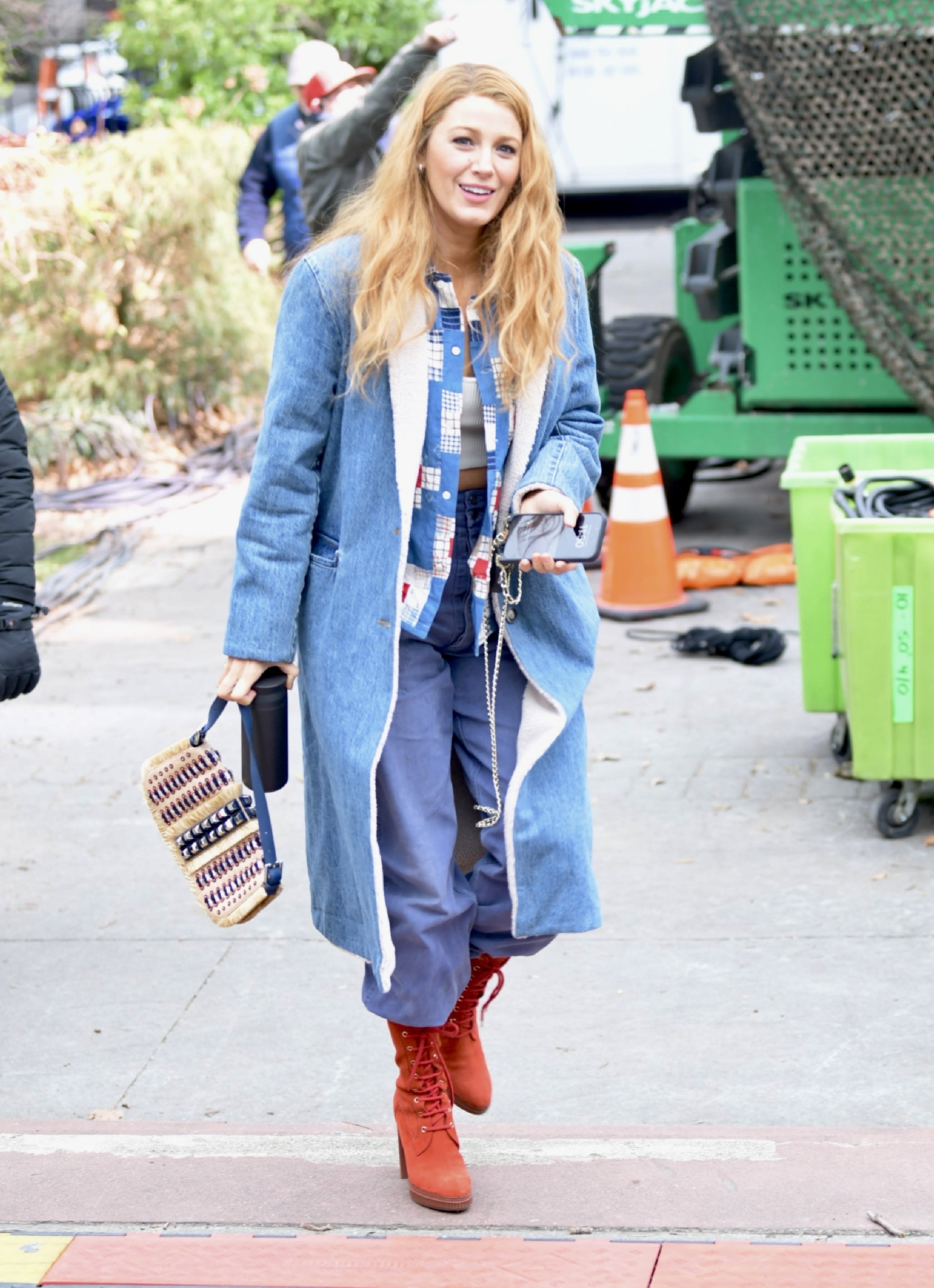 Blake Lively wearing a long coat, patterned scarf, and red boots on a city street