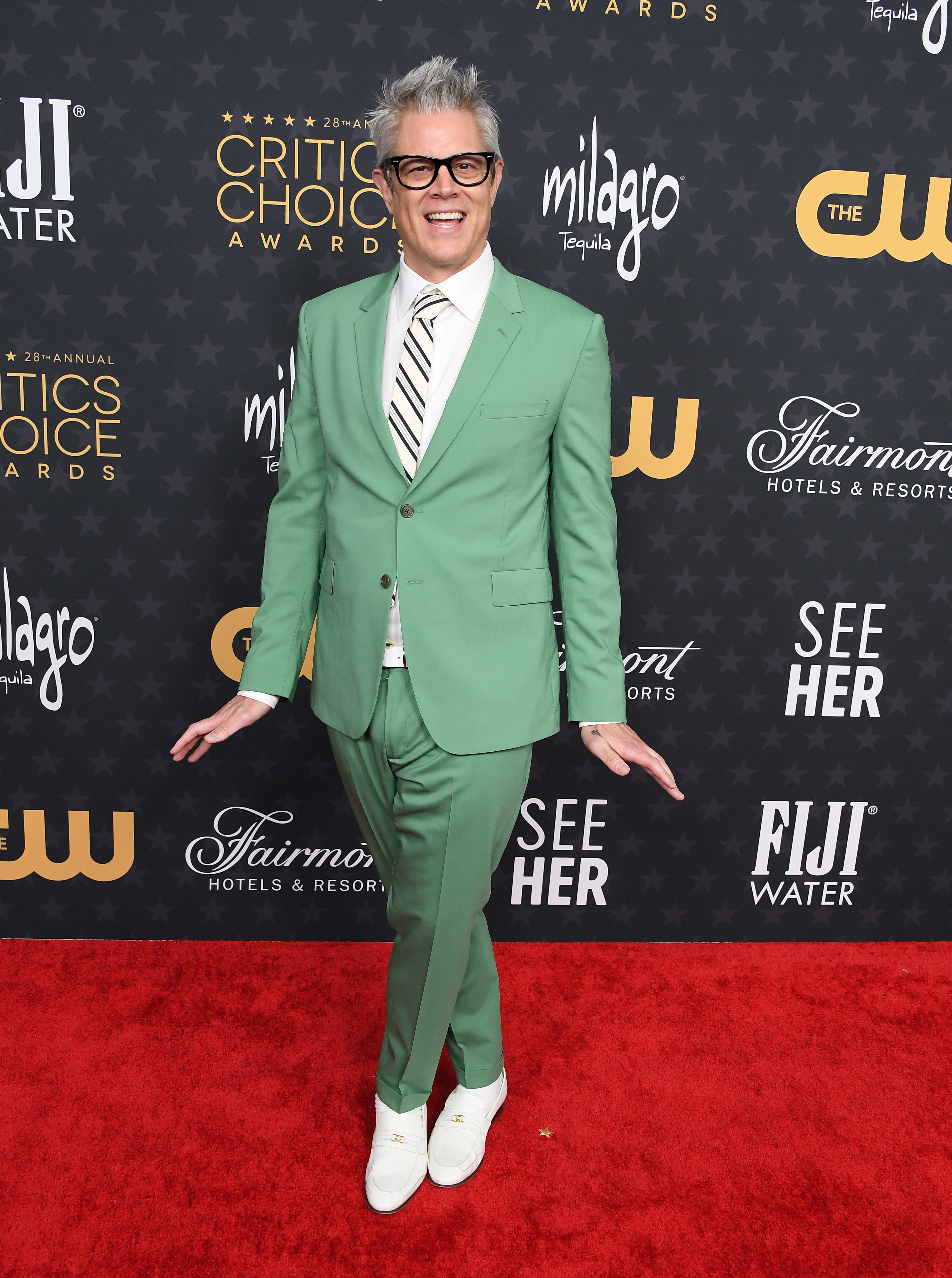 Johnny in ga suit and shoes on red carpet posing with his feet crossed together and hands out to his side at Critics Choice Awards