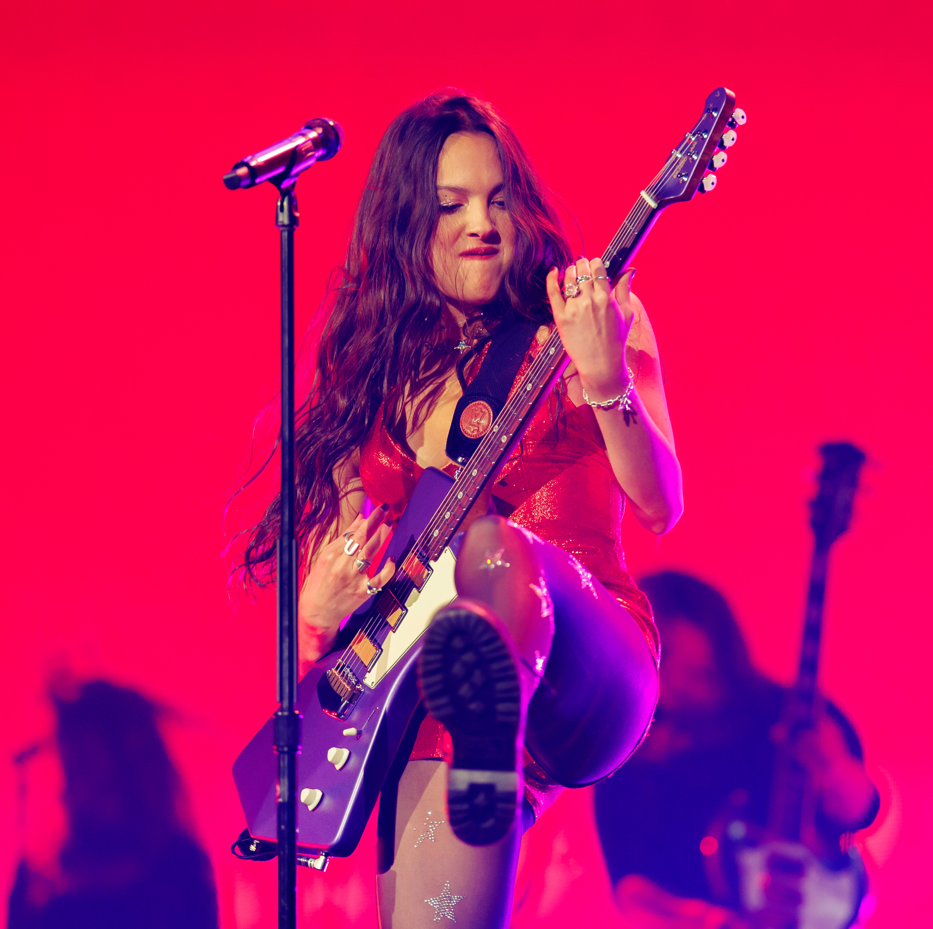 Olivia performing on stage with a guitar, wearing a performance outfit