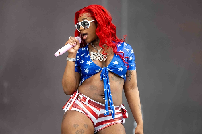 Sexyy Red performing on stage wearing a star-spangled outfit with sunglasses and a microphone