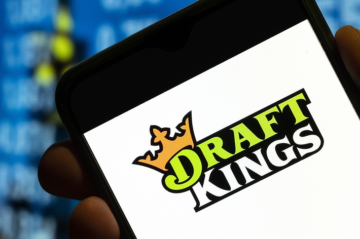Hand holding smartphone displaying DraftKings logo with blurred digital screen in the background