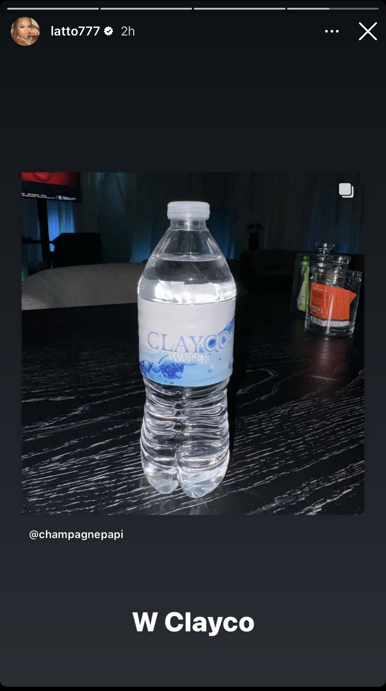 Water bottle on a table tagged with &quot;W Clayco&quot; and a handle mentioning @champagnepapi