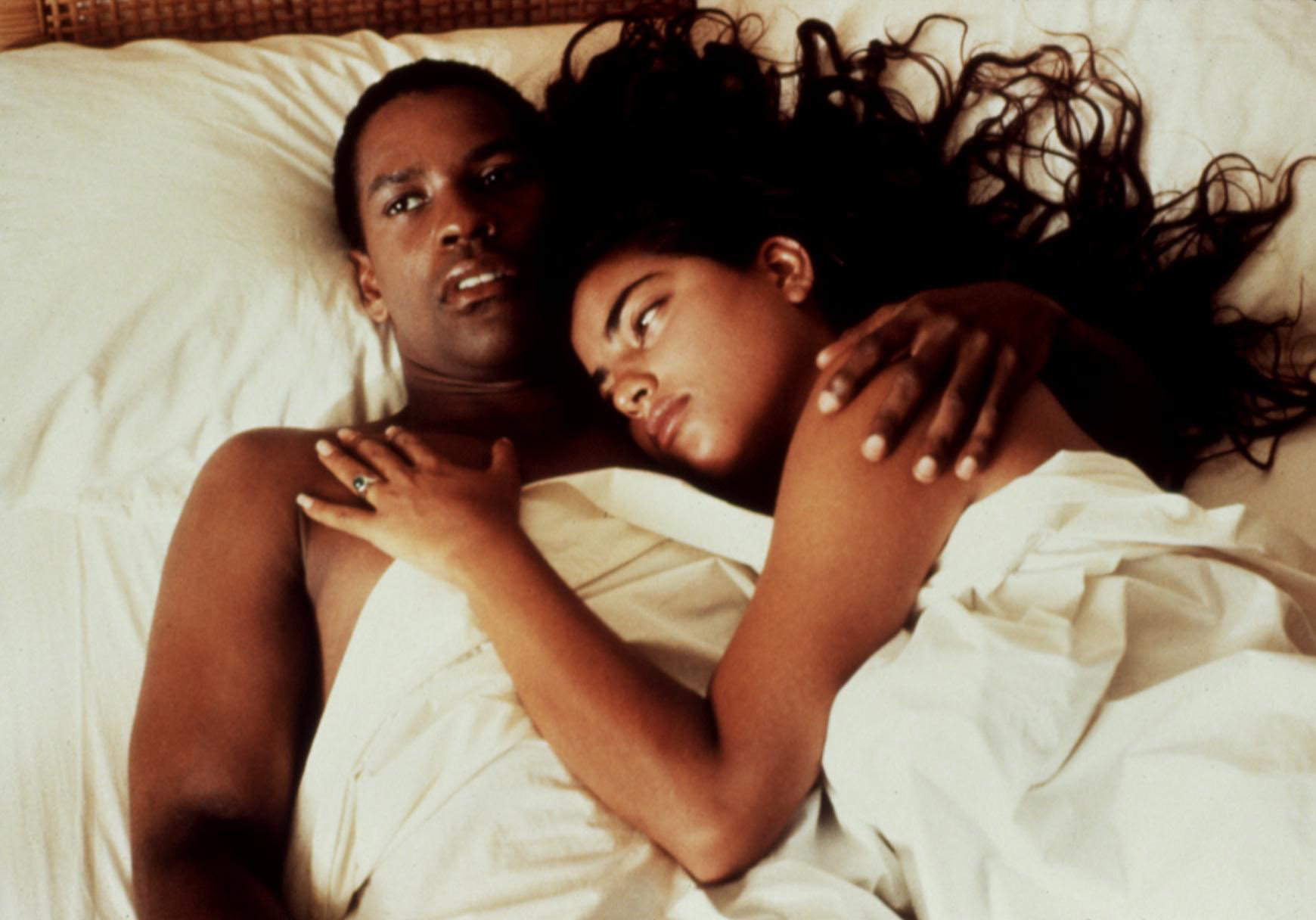 Denzel Washington and Sarita Choudhury in Mississippi Masala lying close together under a white sheet, appearing contemplative