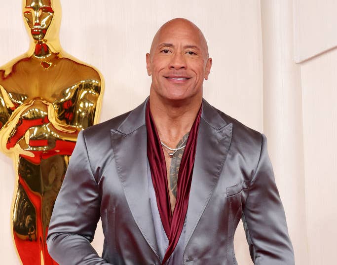 Dwayne Johnson poses in a satin suit with an Oscar statue nearby