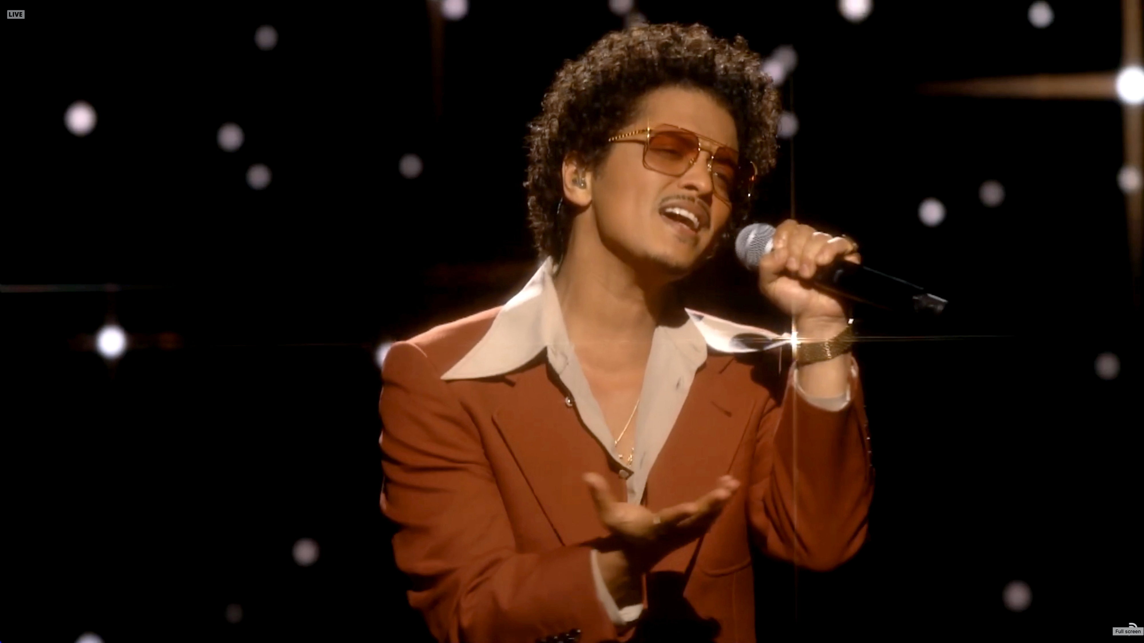 Bruno Mars performs on stage, wearing a velvet jacket, with a microphone in hand