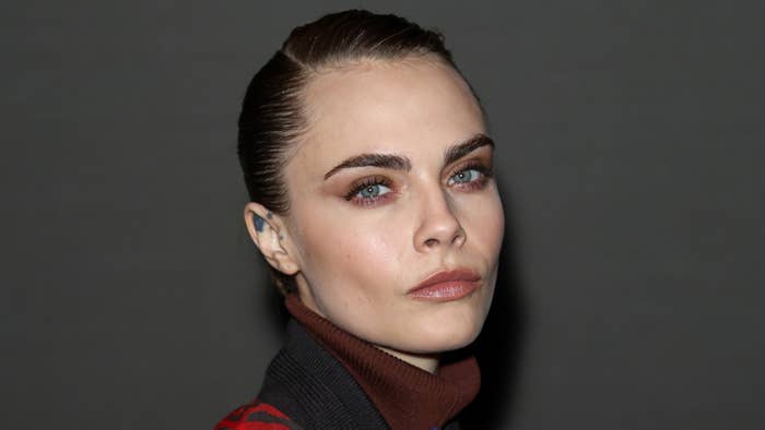 Person with slicked back hair and high-neck top poses for the camera at an event