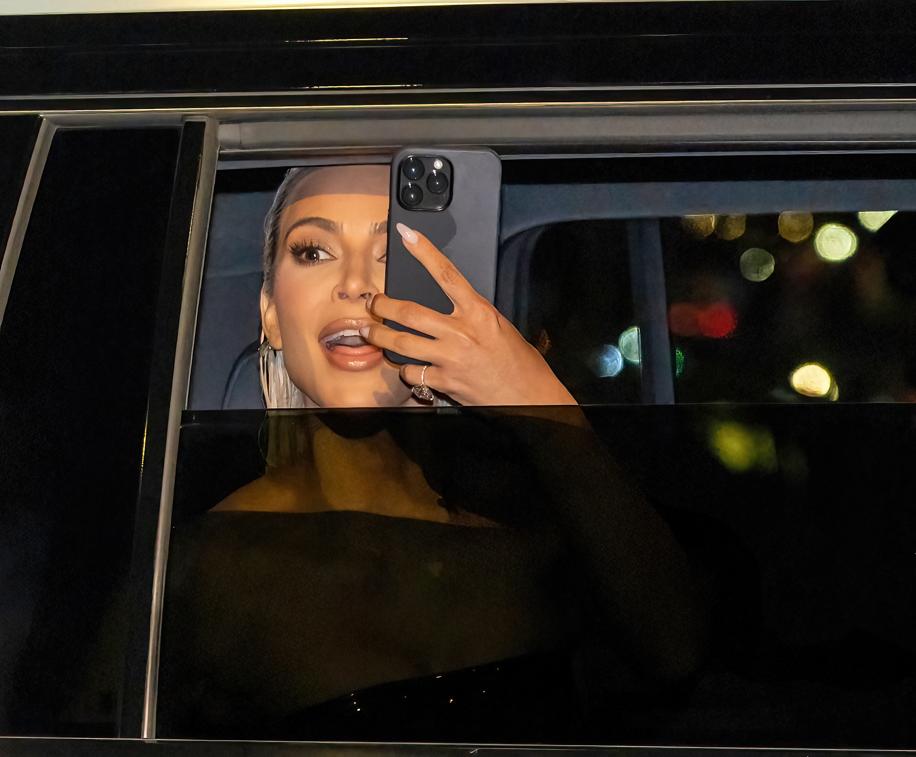 Kim Kardashian taking a selfie in a car, wearing an off-the-shoulder outfit