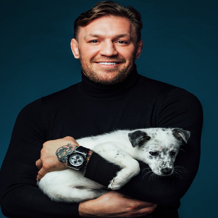 Man in a turtleneck holding a small dog, both facing the camera