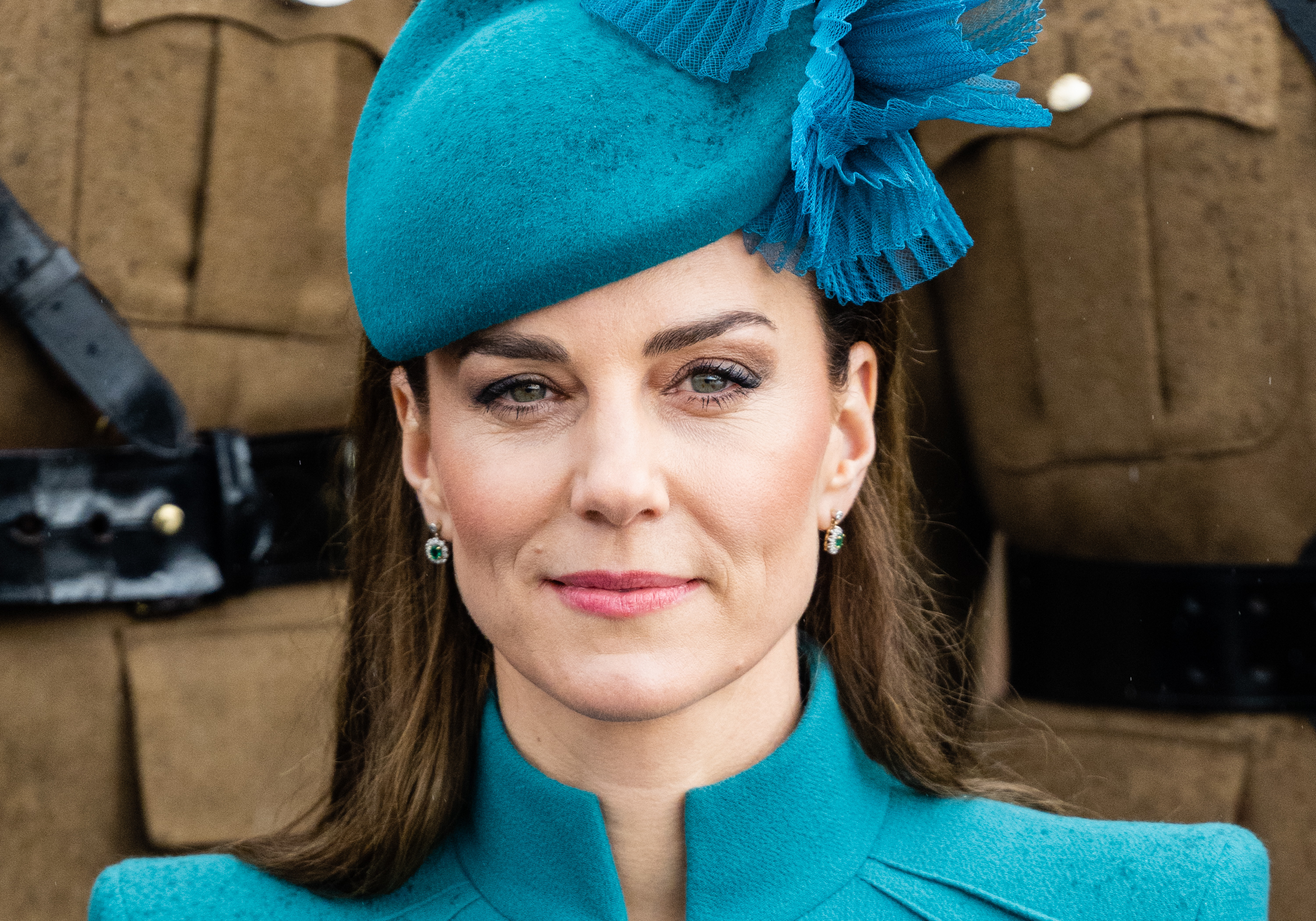 Kate Middleton wearing a fascinatior and matching coat, earrings visible, smiling at an event