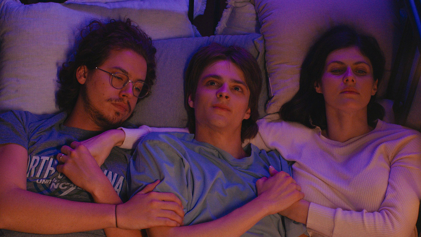 Three actors in a scene, lying side by side, seemingly deep in thought. They portray characters in a casual setting