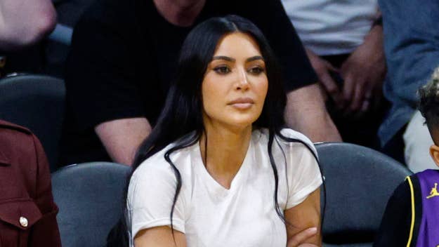 Kim Kardashian seated courtside wearing a casual white top, with focused expression
