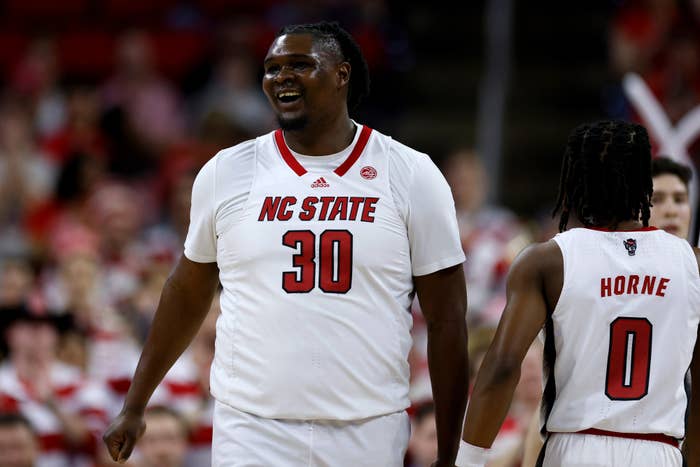 Basketball player in NC State jersey number 30 smiling on the court with teammate number 0
