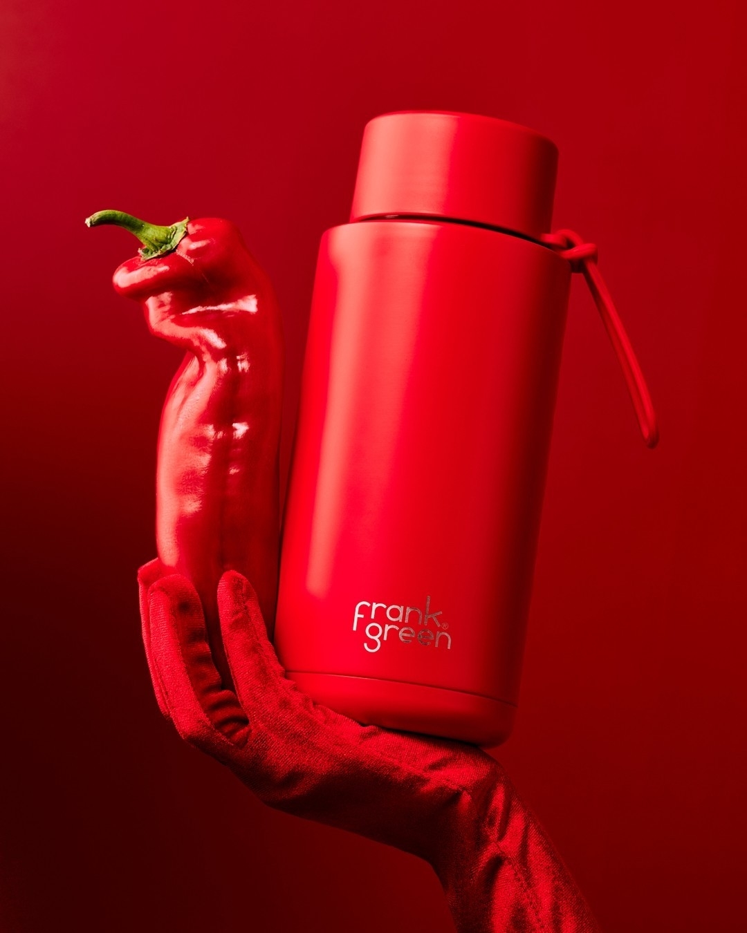 A hand in a red glove holds a red chili and a &#x27;frank green&#x27; branded reusable bottle