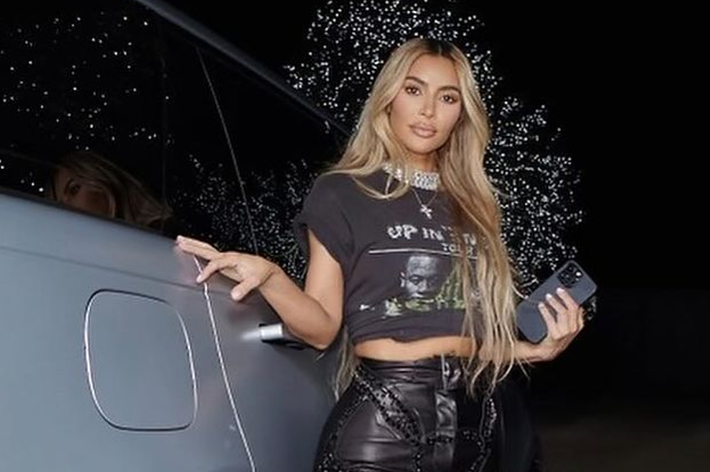Kim Kardashian posing next to a car in a graphic tee and black leather pants