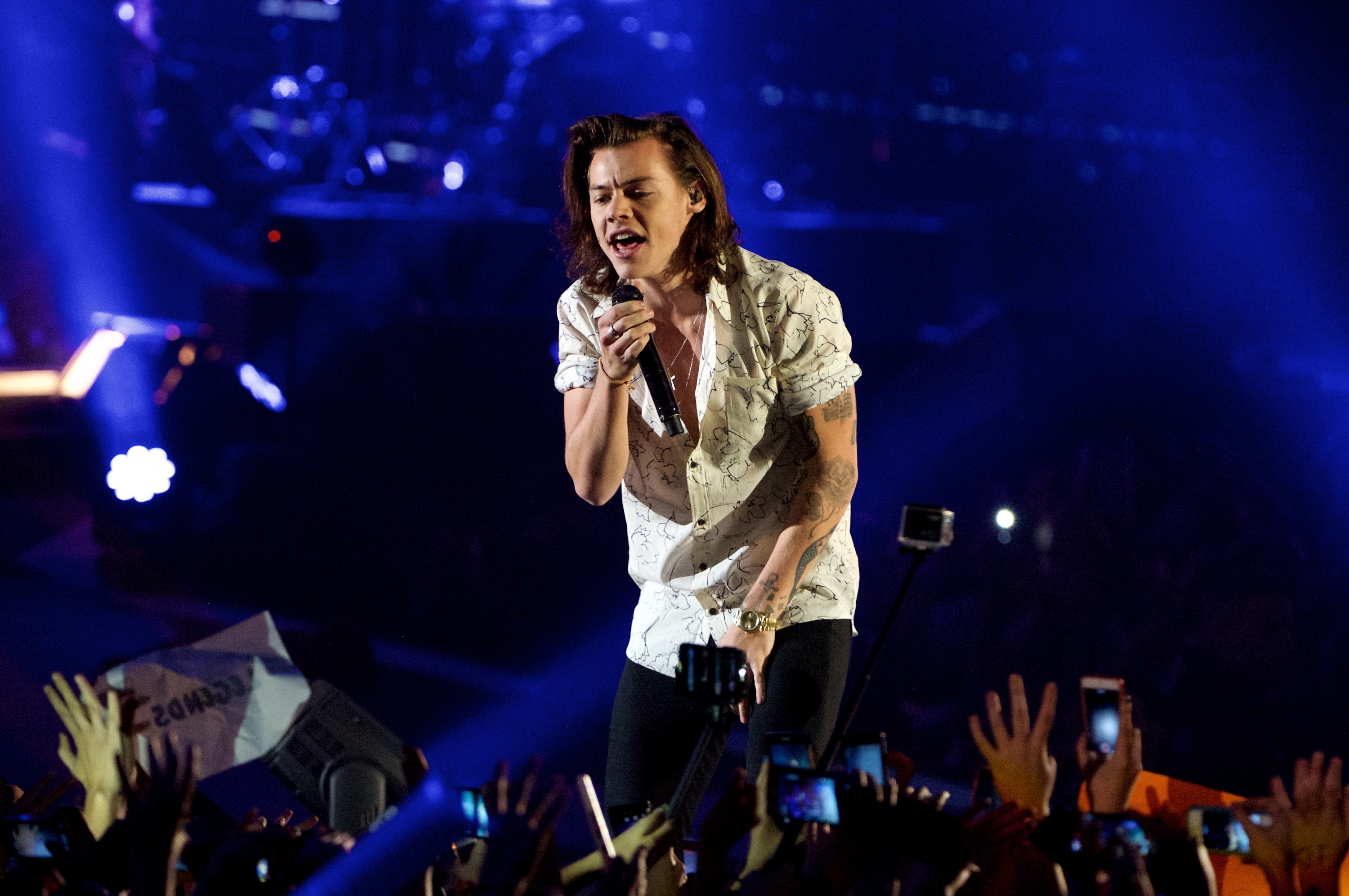 Harry Styles performs onstage in a patterned shirt, surrounded by an audience